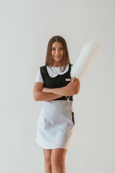 Positive, chambermaid is holding cleaning thing. Young pretty woman is against background in the studio photo