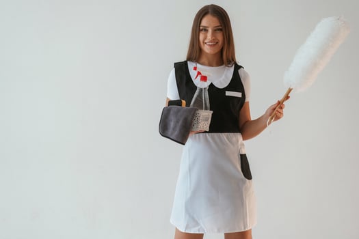 Chambermaid is with ,,cleaning product, and tool. Young pretty woman is against background in the studio photo