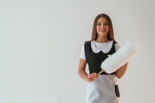Positive, chambermaid is holding cleaning,, thing. Young pretty woman is against background in the studio photo