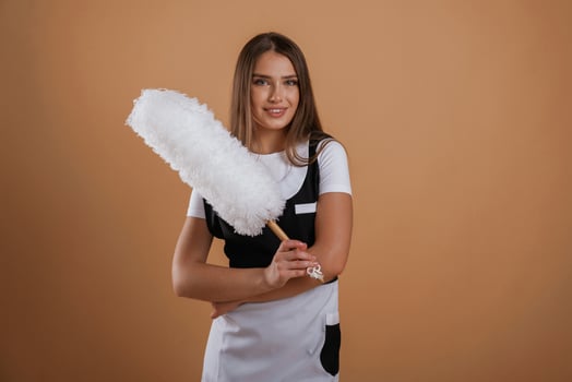 Beautiful, chambermaid is holding cleaning brush. Young pretty woman is against background in the studio photo