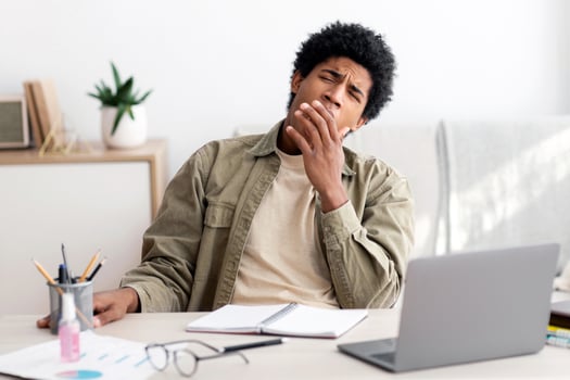 Bored black teen student yawning during his online studies at home. African American adolescent exhausted from preparing for exam or writing coursework feeling sleepy near laptop, indoors photo
