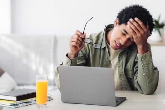 Tired black guy suffering from headache during online studies in front of laptop at home, panorama. Overworked African American teenager with migraine exhausted from doing school assignments photo