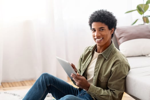 Homeschooling concept. Positive black teen guy with tablet computer studying remotely from home, empty space. Happy teenager taking online educational course, communicating with fellow students on web photo