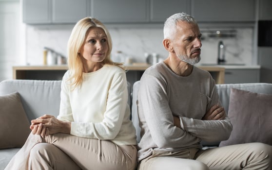 A senior couple appears emotionally distant as they sit on a couch in their living room, highlighting their disagreement. The tension is palpable as they avoid each other's gaze. photo