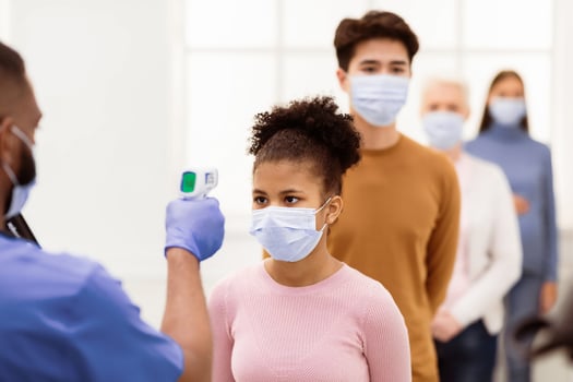 Temperature Screening Concept. Nurse Measuring Fever For Black Patient Girl Standing In Queue Line, Using Infrared Contactless Themometer In Hospital Waiting-Room. Coronavirus Covid-19 Protection photo