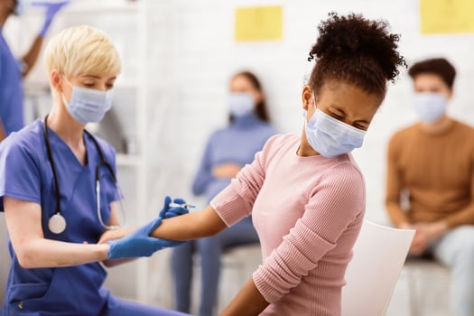 Coronavirus Vaccination. Black Teen Girl Receiving Covid-19 Vaccine Injection In Arm Sitting With Nurse In Hospital Room. Corona Virus Prevention, Cure And Medication Concept. Selective Focus photo