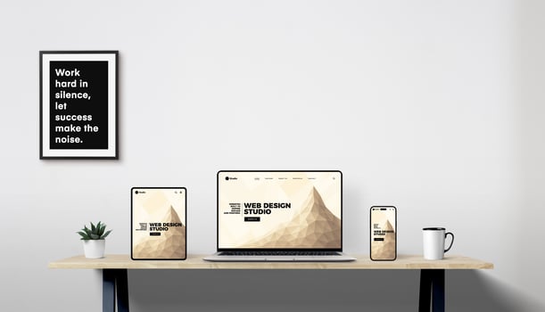 Responsive web design displayed on laptop, tablet, and phone in modern workspace with plant, coffee mug, and framed motivational quote photo