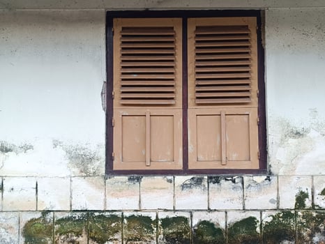 An old wooden window with grilles and panels at the bottom, on an old, mossy building in Indonesia. photo