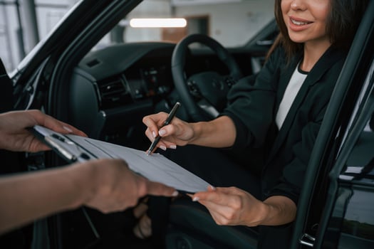 Process of buying new car, ,,woman is signing documents while sitting in a new automobile photo
