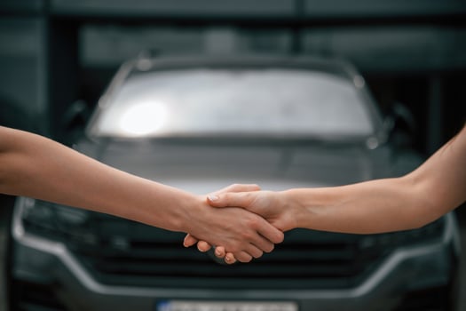 Side, close up view of handshake of two women against car photo