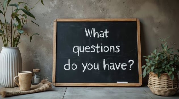 chalkboard displays the question 'What questions do you have' with a vase and plant in the background. photo
