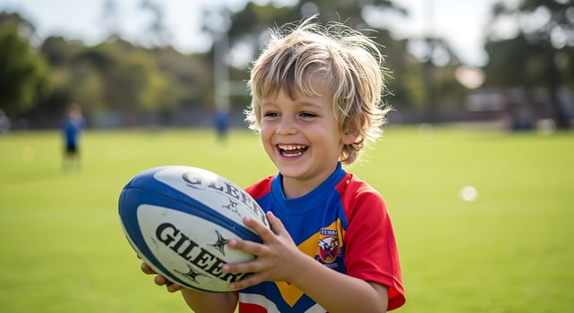 A young boy smiles while holding a rugby ball photo