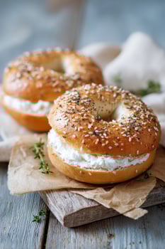 Freshly baked sesame bagels filled with creamy cheese spread, placed on rustic wooden board, surrounded by soft fabric and herbs, showcasing delicious breakfast option photo