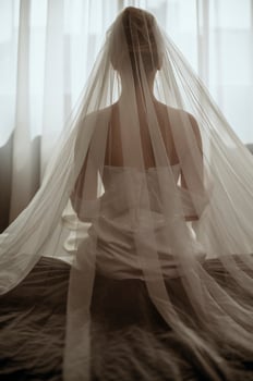 Close-up of a bride in a luxurious veil from the back. The bride in a white dress is sitting on a bed, she is wearing a large veil. Silhouette of a bride, view from the back photo