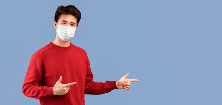 Special Offer. Asian guy in face mask pointing his fingers away at copy space for your text or logo, isolated over studio background wall, banner, panorama. Man showing place for advert photo