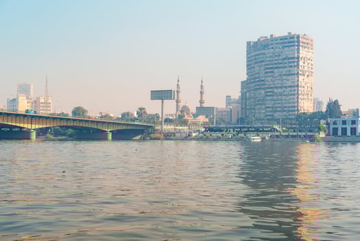 View of Cairo skyline with mosques, buildings, and a bridge reflected in the Nile River during the golden hour photo