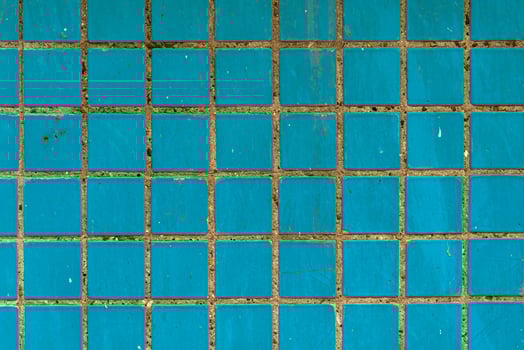 Square blue ceramic tiles with worn grout and surface scratches, creating a gritty, urban wall texture for design and architectural backgrounds. photo