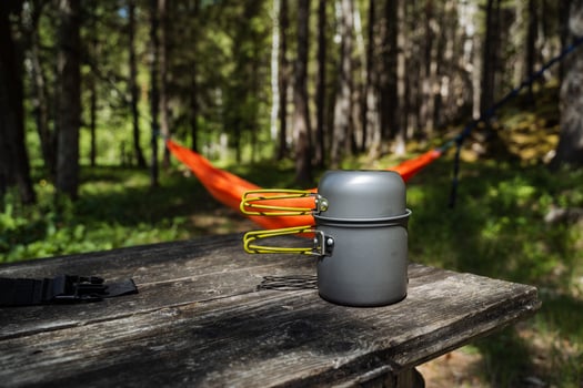 An old, wellloved pot is resting on a rustic wooden table situated in a tranquil woodland area, next to a gently swaying hammock that dances in the cool breeze, surrounded by tall trees photo