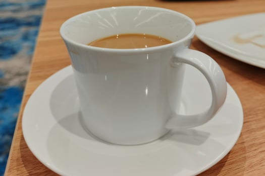 A white cup of coffee on a saucer, placed on a wooden table. photo