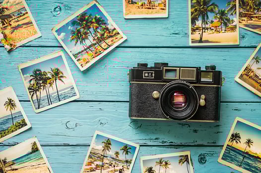 Vintage camera lying on light blue table surrounded by beach photos