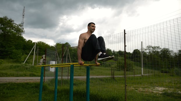 Strong guy trainin abdominal muscles on parallel bars at sports ground. Young shirtless sportsman exercising at nature. Sporty athlete working out at nature. Concept of active sportive lifestyle photo