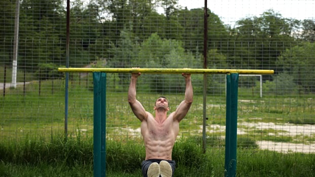 Hard shirtless sportsman doing exercises on parallel bars at nature. Strong and muscular man working out at sports ground. Young athletic guy exercising outdoor. Concept of active healthy lifestyle photo