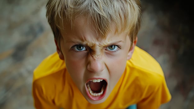 Young boy expressing intense anger in a bright yellow shirt in a natural indoor setting during daylight photo