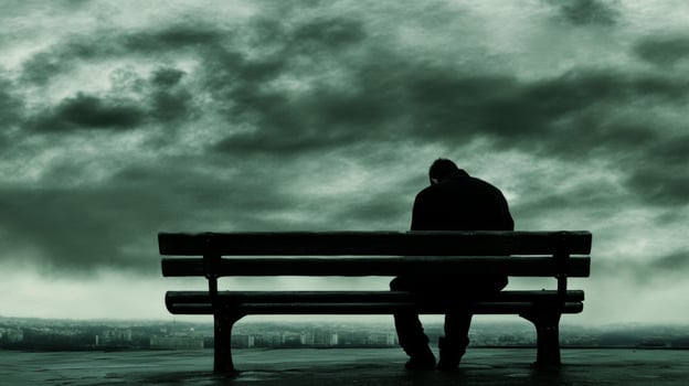 Man sitting alone on a bench under a dramatic sky in an urban area during twilight hours photo