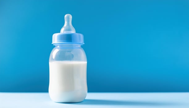 Plastic baby milk bottle on blue backdrop. Feeding time. photo