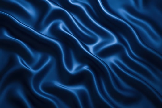 A close-up view of deep blue satin fabric with smooth, flowing folds. The texture appears soft and luxurious, showcasing the sheen of the material. photo