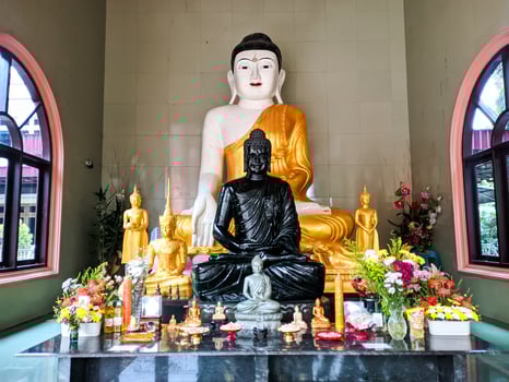 Buddha altar in a Buddhist place of worship with a white and gold main statue. The main Buddha statue is surrounded by flowers, incense and several other small Buddha statues. photo