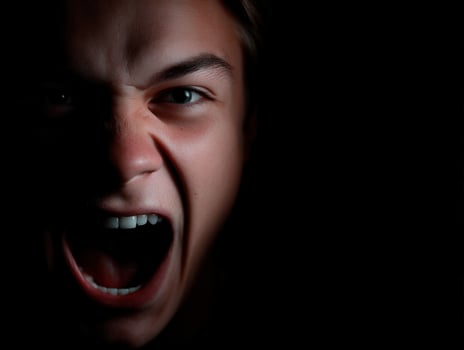 Teenager shows anger by yelling intensely on black background photo