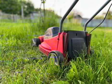 Red lawn mower cutting green grass in garden during summer day. photo