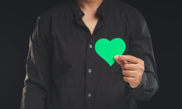 Hand holding a green heart shape symbol while standing against a black background. photo