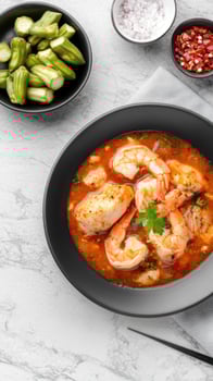 Shrimp and fish gumbo served on marble table, okra and spices near. Blog cooking idea photo