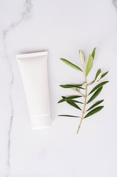 Top view of white plastic tube without label and olive branch on white marble background photo