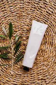 Top view of white tube without label and olive branch on wicker beige background photo