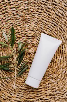 Top view of white plastic tube without label and olive branch on wicker beige background photo