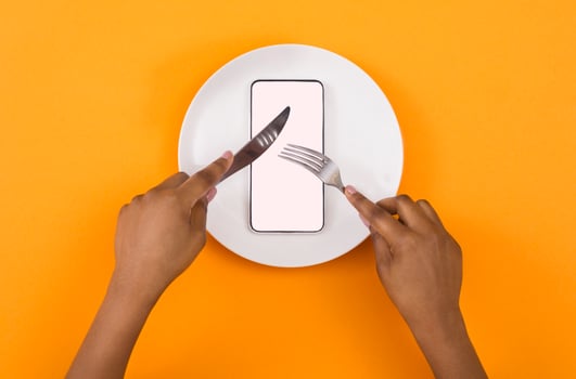 Absorption of information. African american woman eating blank smartphone with knife and fork, top view, mockup photo