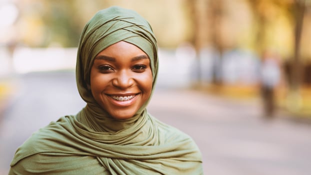 Black Muslim Woman With Braces On Teeth Smiling To Camera Posing Standing Outdoors, Wearing Traditional Hijab Headscarf. Portrait Of Modern Islamic Young Lady. Panorama With Free Space photo