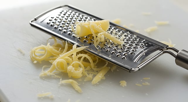 Grating Yellow Cheese with Metal Grater on White Board photo