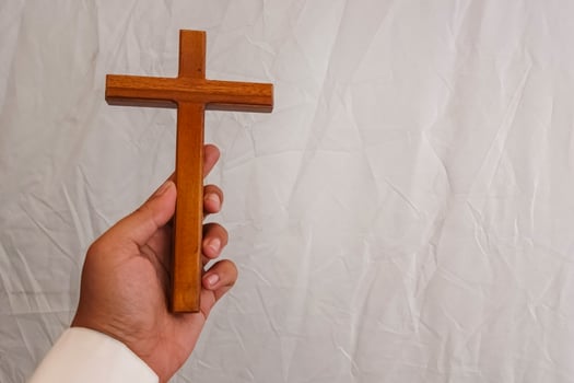 A hand holds a wooden cross against a white wrinkled background. photo