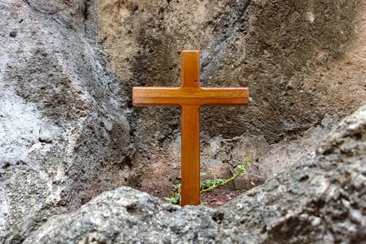 A wooden cross stands among rocks against a rough stone wall background. photo