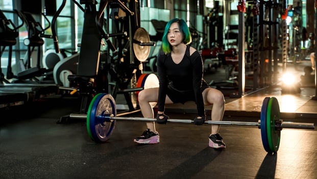 Strong young woman preparing for sumo deadlift with heavy barbell in gym, wearing black athletic outfit, focus and power in strength training photo