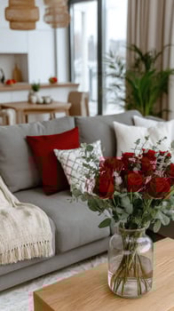 A vase of red roses sits on a table in front of a couch photo