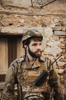 Soldier In Uniform Checks The Walls Of Destroyed Houses In The City photo