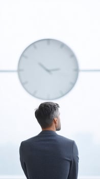 Man in formal attire gazing at large wall clock in modern office space, reflecting on time and productivity in a minimalist environment photo