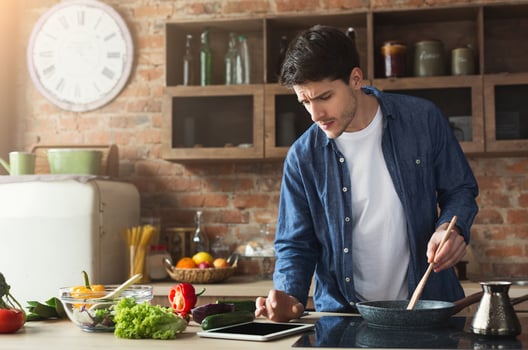 Happy man cooking healthy food with recipe, looking on digital tablet in loft kitchen at home on sunny day. Preparing vegetable salad. photo