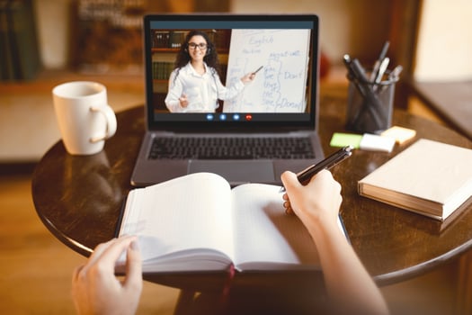 Online Course Concept. Point of view of female student sitting at table, writing in notebook, taking notes, using laptop, having online class with English teacher. Remote distant studying from home photo