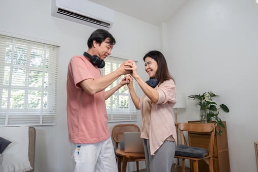 Happy middle-aged couple dancing together and holding hands indoors with headphones. photo